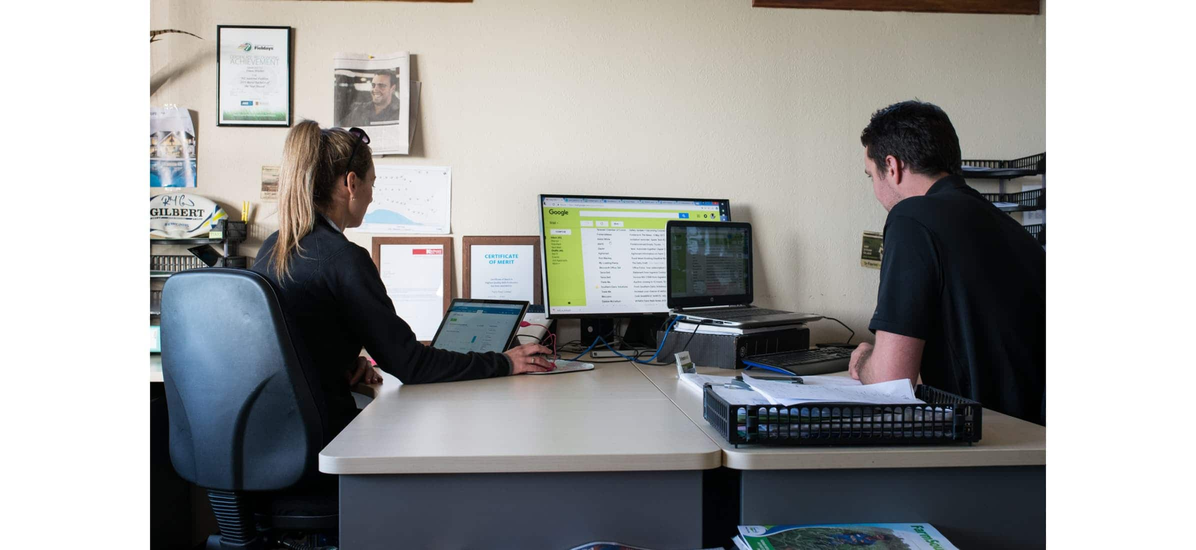 Simon and Monica sit at their office desk together working on computers.